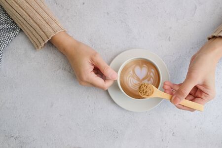 woman put brown sugar in the latte art coffee . flatlay design . health diet and diabetes.の写真素材
