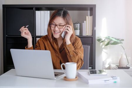 asian adult entrepreneur smiling and work on laptop and mobile phone with paperwork in the smart officeの写真素材