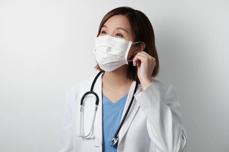 asian doctor smile under the medical mask to protect and fight infection from germ, bacteria, covid19, corona , sars , influenza virus on white background.の写真素材
