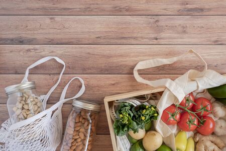 Cotton eco net bag with fresh vegetables in the pine wood box and sustainable glass jar on wooden table flat lay.plastic free for groceries product shopping and delivery. zero waste lifestyle .の写真素材