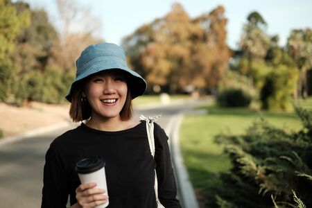 asian woman in the park smiling and holding the biodegradable coffee cup.の写真素材