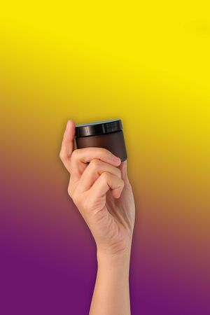 hand hold cosmetic skincare cream amber glass jar on colorful background.の写真素材