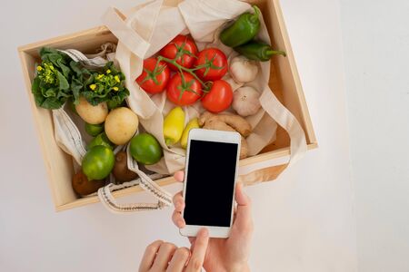 mobile phone with the eco bag and fresh vegetable in wood box. online grocery and organic farmer product shopping application. food and cooking recipe or nutrition counting.flat lay.の写真素材