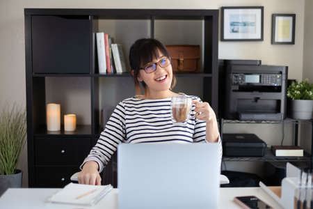 college student learning online class looking at the camera on computer screen. remote course for university education. happy and smile asian woman.の写真素材