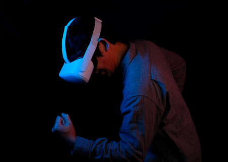 Asian man is using the virtual reality for playing game d entertainment. He posting winning gesture. Neon theme black background.の写真素材