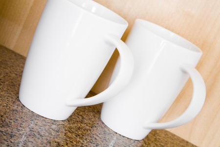 Two white mugs on a counter against a wooden wallの写真素材