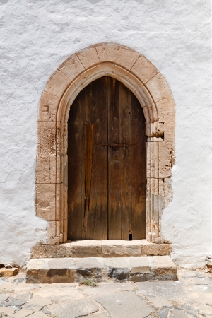 Ancient wooden arched door with stone archway and stucco white wallの写真素材