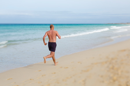 Middle aged man jogging in summer on a beachの写真素材
