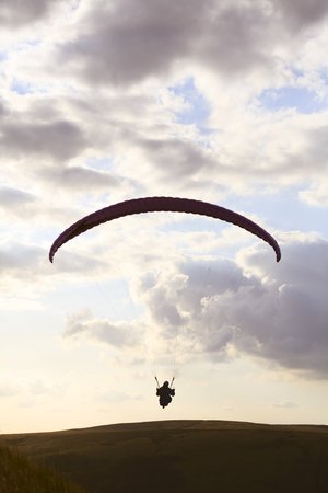 A paraglider is silhouetted against the sky over Edale Valley in the Peak District, Derbyshire. The pilots gain lift from the strong updraft that occurs on windward hill slopes.の写真素材