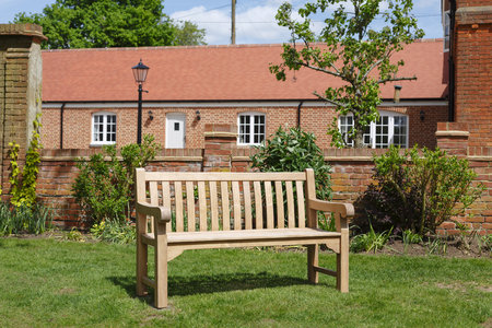 Teak hardwood bench on a lawn in an English garden with historic Victorian home in the backgroundの写真素材