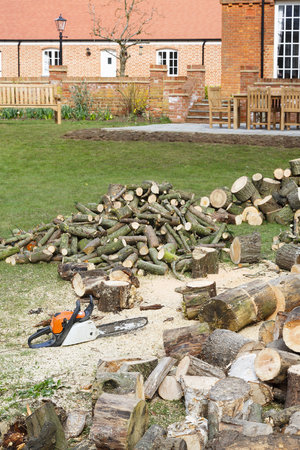 Cutting firewood with a chainsaw in an English garden setting with a large country house in the backgroundの写真素材