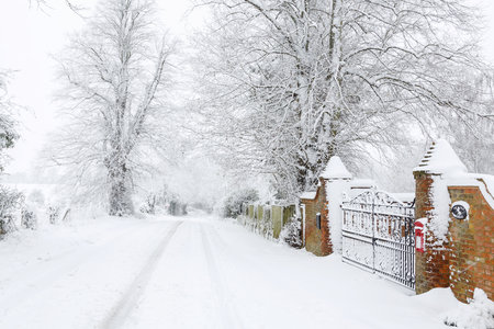 Snow covered British road outside entrance to an old house surrounded by countryside in winterの写真素材