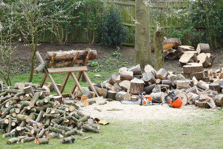 Firewood on a saw horse with chainsaw next to piles of firewood in a garden settingの写真素材