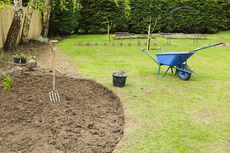 Preparing a freshly dug flower bed for planting in a garden with fork and wheelbarrowの写真素材