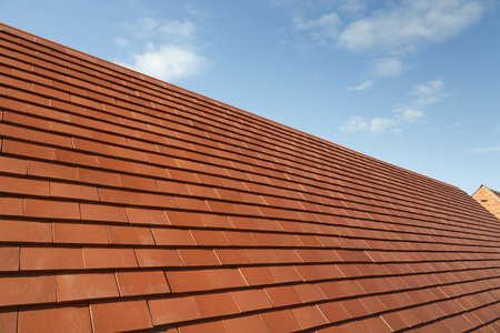 New traditional plain clay tiles on a house roof against a blue sky with copy spaceの写真素材