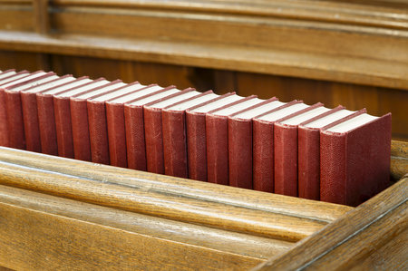 Closeup of a row of red hymn books on an old wooden church pew. Depicts religion and prayer