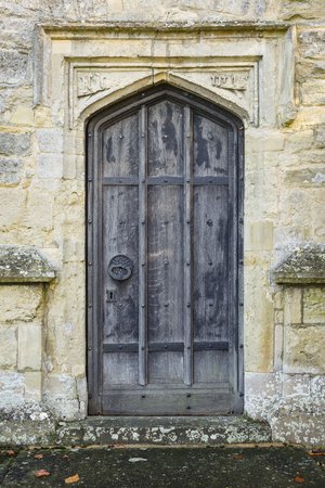 Ancient arched wooden door in entrance to an old medieval stone church in Englandの写真素材