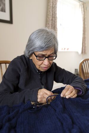 An old woman of Indian Asian ethnicity knitting in an English homeの写真素材