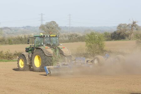 Buckingham, UK - April 01, 2019. A John Deere tractor cultivates land during a drought using a Cambridge roller or cultipacker. Buckingham, UKのeditorial素材