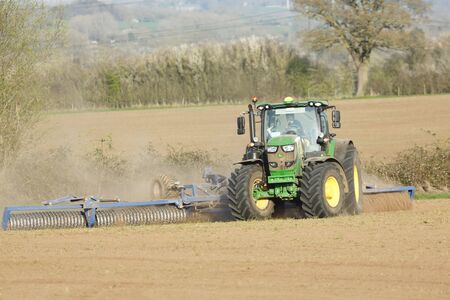 Buckingham, UK - April 01, 2019. A farmer drives a John Deere tractor to cultivate land during a drought, using a Cambridge roller or cultipacker.のeditorial素材
