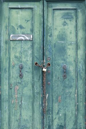 Old locked door with peeling paint, padlock and chain in Venice, Italyの写真素材