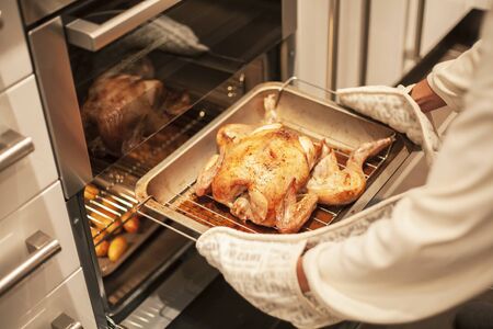 Woman cooking roast chicken in an oven