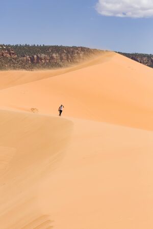 Asian Indian woman walks alone in high winds along a huge sand dune in Coral Pink Sand Dunes State Park, Utah, USAの写真素材