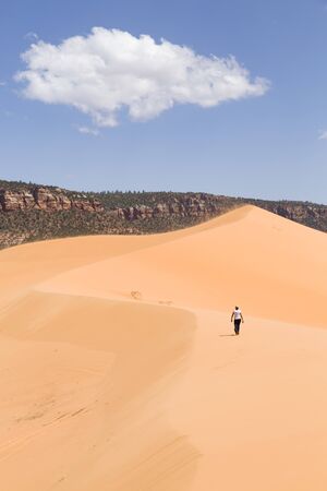Young woman walks alone in desert landscape, Coral Pink Sand Dunes, Utah, USAの写真素材