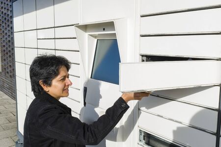 British Asian woman using an automated postal locker, parcel collection point in UK