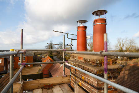 Repairing chimney pots with scaffolding on a roof. Construction work on a house renovation, UKの写真素材