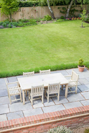 Large back garden in UK in summer, with wooden furniture on a garden patio terrace