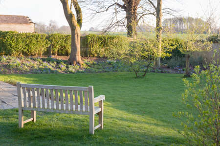 Large UK back garden in winter with a wooden garden bench on lawn, with a view of Buckinghamshire countrysideの写真素材