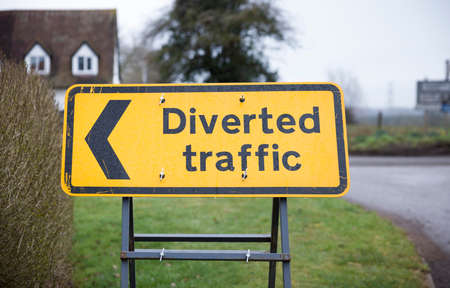 Diverted traffic sign with left arrow. Yellow UK road sign closeup showing a diversion or detour.の写真素材