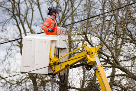 BUCKINGHAM, UK - March 25, 2021. Utility worker in a cherry picker cutting back trees near overhead power lines, UKのeditorial素材