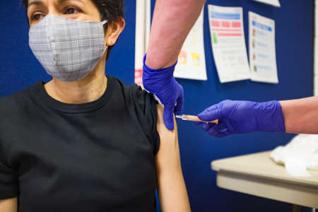 British Asian woman wearing a face mask, getting a Covid 19 vaccine at a vaccination centre in...