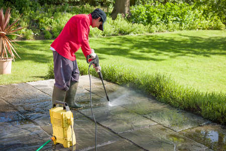 Jet washing a patio. Woman high pressure washing, power washing or cleaning a garden terrace, UKの写真素材