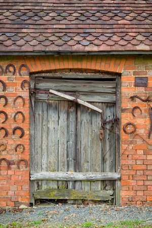 Old stable building with wooden stable door. Wall decorated with horseshoes, UKの写真素材