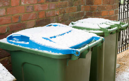 Green and blue wheelie bins in a garden in winter, UK. Bin lids covered in snow.の写真素材
