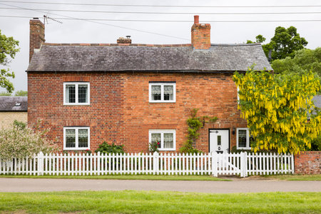 NORTHAMPTONSHIRE, UK - May 25, 2022. Old brick cottage with white picket fenceのeditorial素材