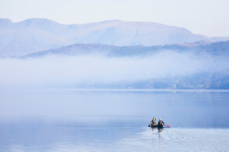 LAKE DISTRICT, UK - October 12, 2010. Couple paddling a double canoe on a lake, misty morning in autumn. Coniston Water, Lake District, England, UKのeditorial素材