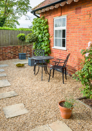UK garden patio design. Hard landscaping with York stone stepping stones in gravel and a metal bistro table and chairs.の写真素材