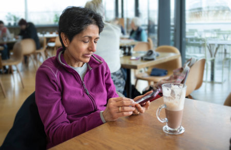 Middle aged Indian Asian woman sitting alone in a coffee shop cafe using a mobile phone, Oxford, UKの写真素材