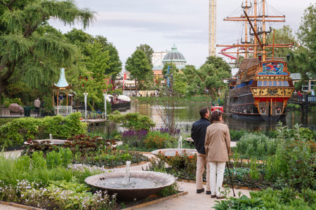 COPENHAGEN, DENMARK - June 17, 2006. Mature couple visiting Tivoli Gardens with lake and pirate ship. Copenhagen, Denmark.のeditorial素材