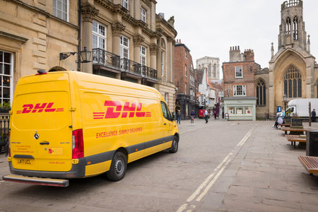 YORK, UK - April 19, 2023. Yellow DHL delivery van, courier driving through city centre.のeditorial素材