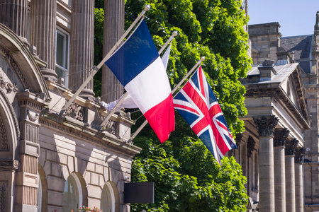 French flag and Union Jack flying side by side on flagpoles outside a historic building in...