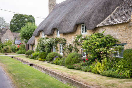 A traditional thatched cottage with stone walls and lush gardens in Minster Lovell, a charming Oxfordshire village in the Cotswolds UKの写真素材