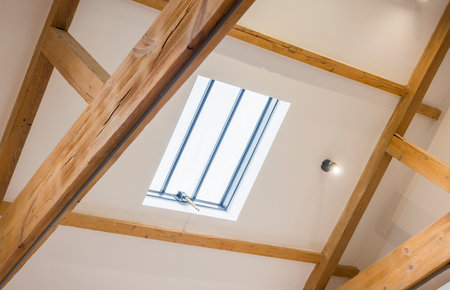 Skylight roof window set in a white sloped ceiling with exposed oak beams in a historic UK home, creating a bright loft spaceの写真素材