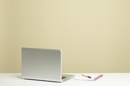 Open laptop on white desk with note pad and penの写真素材