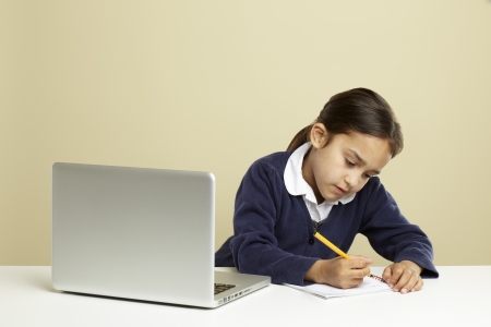 Young girl using laptop on white desk with homeworkの写真素材