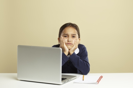 Young girl using laptop on white desk with homework looking boredの写真素材